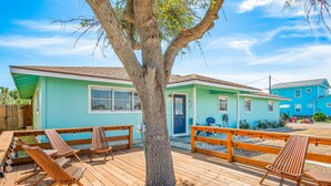 A wooden deck with lounge chairs, a tree, and a building with a blue exterior. - Throw Em Back Inn, Dog Friendly! (Port Aransas)