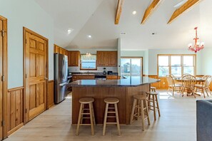 Una cocina amplia con armarios de madera, una isla central con taburetes y un comedor con un ventanal grande.