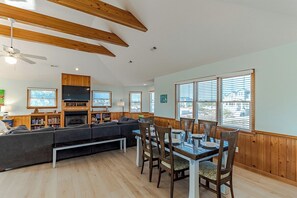 A spacious living area with a sectional sofa, dining table, and chairs, wooden beams on the ceiling, and large windows with blinds. - Oceanside Home w/ Large Private Pool, Hot Tub, & Rec Room (Corolla)