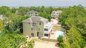 A two-story house with a large front yard, a swimming pool, and a view of the ocean. - Spacious Oceanside Home w/ Pool, Hot Tub, Tiki Bar, & Rec Room (Corolla)
