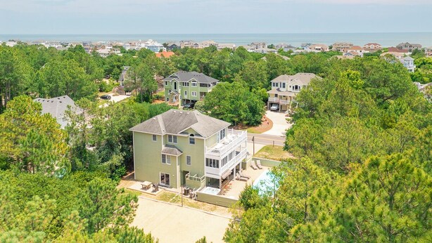A residential area with houses surrounded by trees and a view of the ocean. - Spacious Oceanside Home w/ Pool, Hot Tub, Tiki Bar, & Rec Room (Corolla)