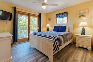 Ein Schlafzimmer mit einem Bett, zwei Nachttischen, einem Deckenventilator, einem Fernseher und einem Fenster mit Vorhängen.