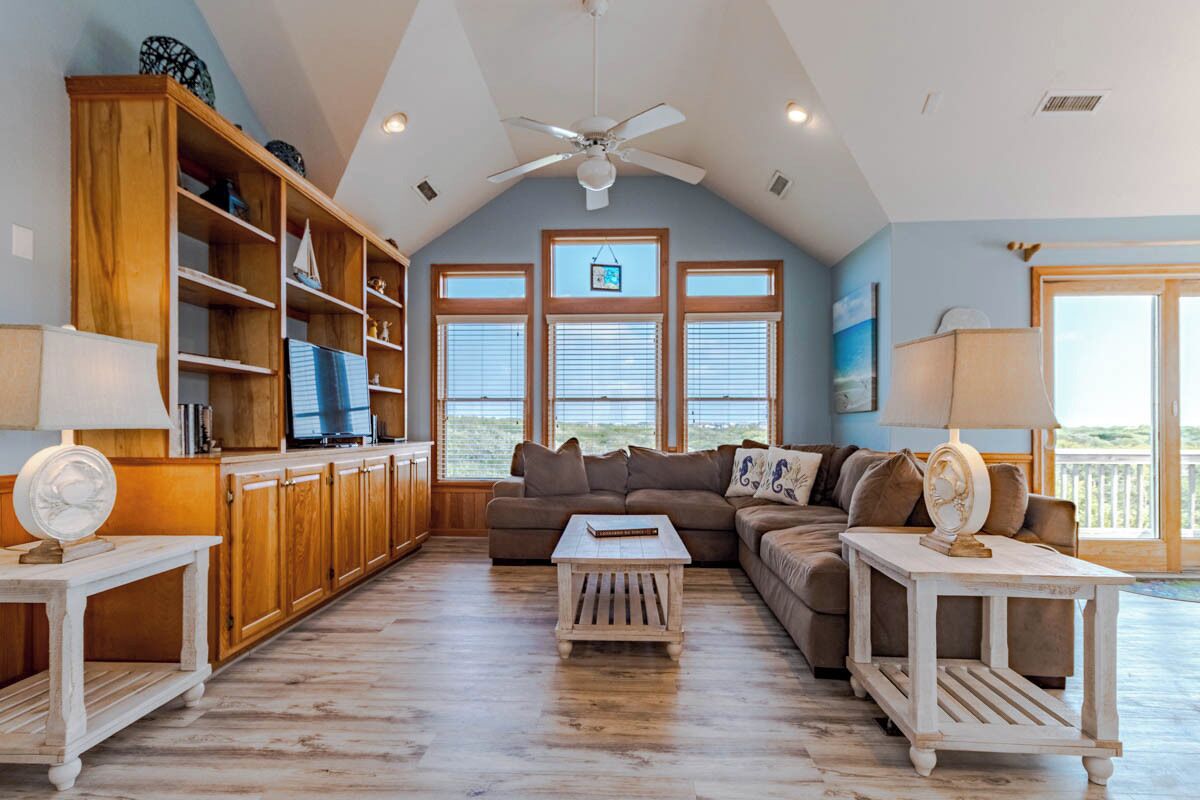 A spacious living room with a high ceiling, wooden cabinets, a sectional sofa, and a ceiling fan.