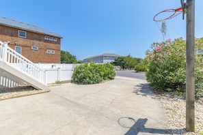 Une allée menant à une maison, avec un panier de basketball, un escalier et une clôture en bois.
