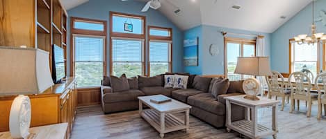 A spacious living room with a large sectional sofa, wooden coffee tables, and a ceiling fan.