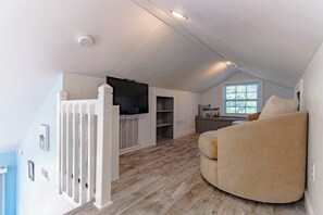 A spacious loft with a high ceiling, a built-in fireplace, a curved beige sofa, and a window providing natural light.