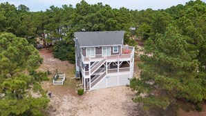 A two-story house with a balcony, surrounded by dense pine trees. - Pet-Friendly Oceanside Home on the Beautiful 4x4 Beaches (Carova)