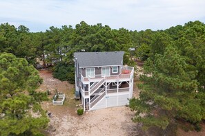 A two-story house with a balcony, surrounded by dense pine trees. - Pet-Friendly Oceanside Home on the Beautiful 4x4 Beaches (Carova)