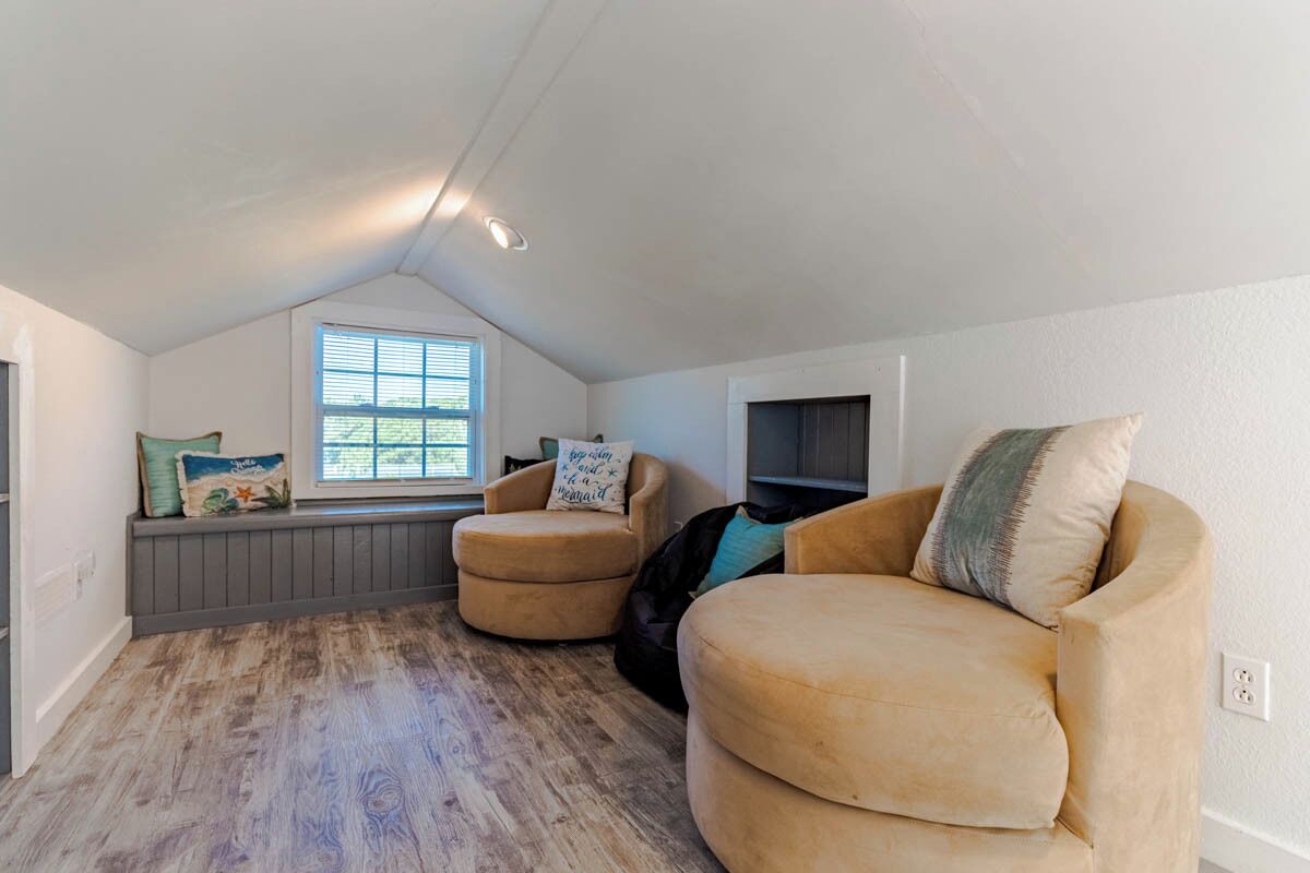 A cozy attic room with a sloped ceiling, a window with blinds, a built-in bench, and a large beige sofa.