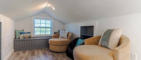 A cozy attic room with a sloped ceiling, a window with blinds, a built-in bench, and a large beige sofa.