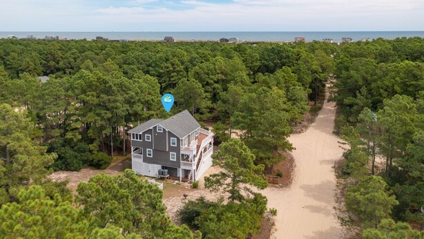 A two-story house surrounded by dense pine trees, with a sandy path leading to the beach. - Pet-Friendly Oceanside Home on the Beautiful 4x4 Beaches (Carova)