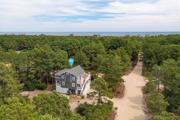 A two-story house surrounded by dense pine trees, with a sandy path leading to the beach. - Pet-Friendly Oceanside Home on the Beautiful 4x4 Beaches (Carova)