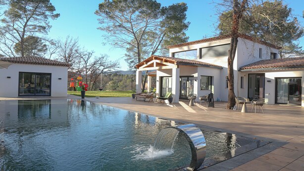 Une maison moderne dotée d’une piscine, d’un espace salon extérieur et offrant une vue sur un parc.