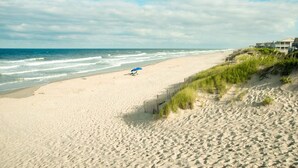 A beach with a wooden fence and a house in the background.