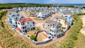 A coastal residential area with multi-story houses, a central road, and a beach in the background.