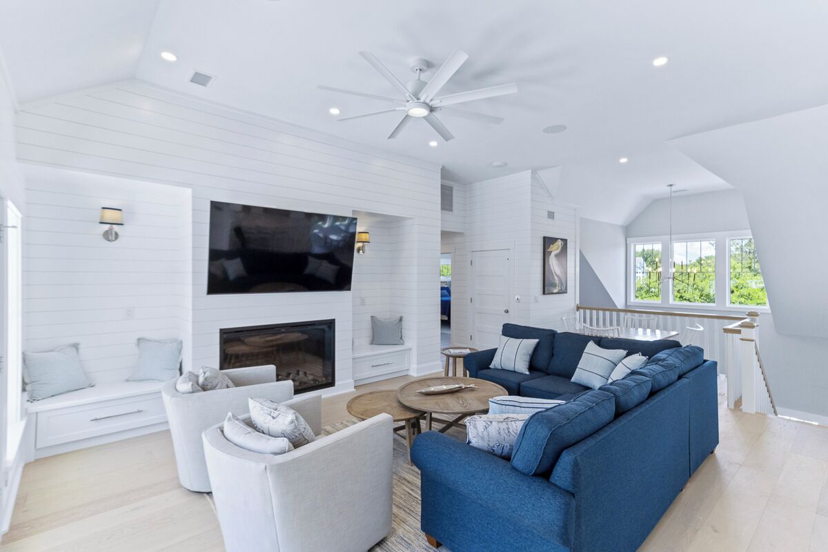 A spacious living room with a fireplace, a large TV mounted on the wall, and a ceiling fan.