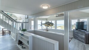Amplia sala de estar con vista al océano, una escalera de madera y una gran decoración con forma de pez.