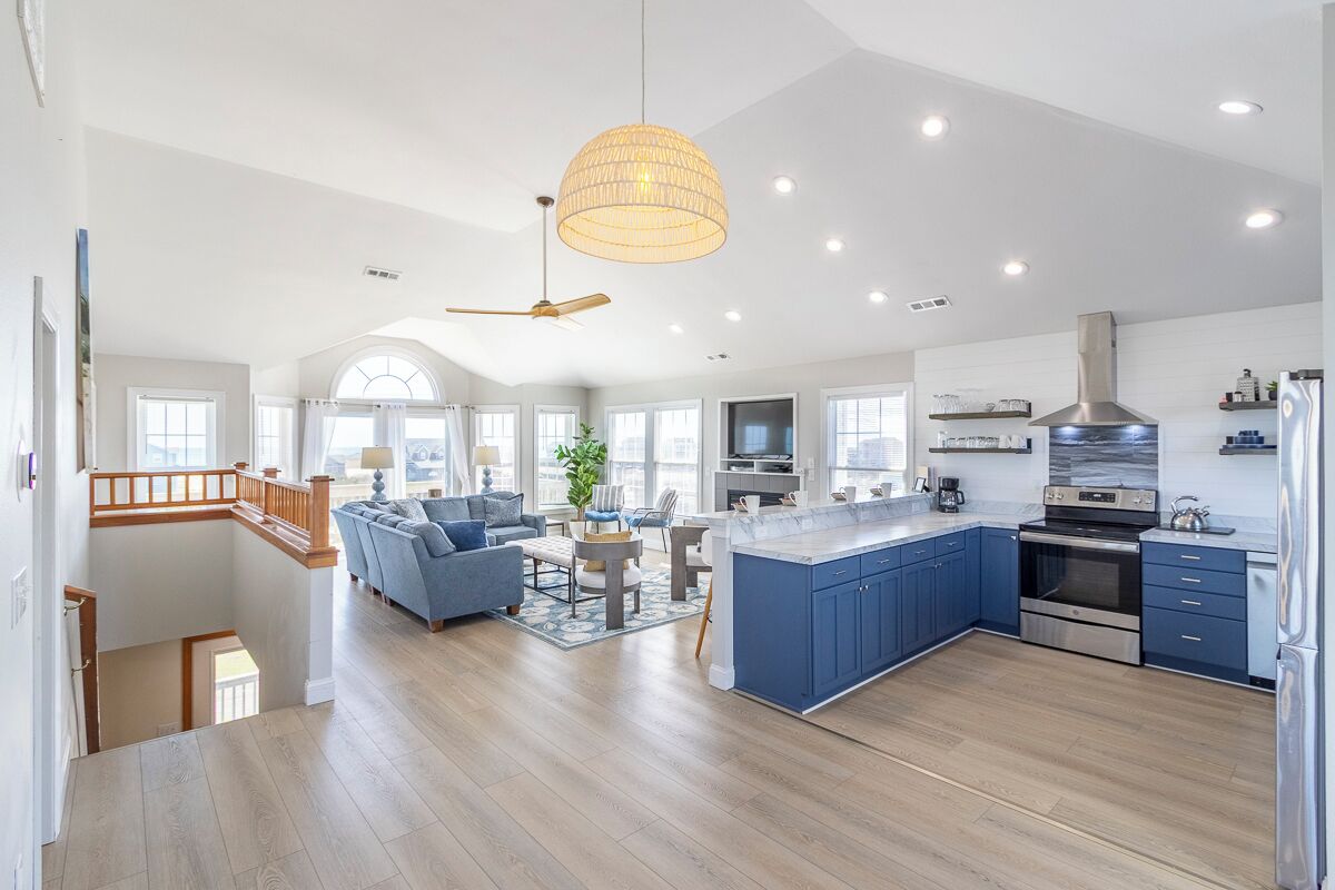 A spacious kitchen with a central island, a dining area with blue furniture, and a staircase leading to an upper level.