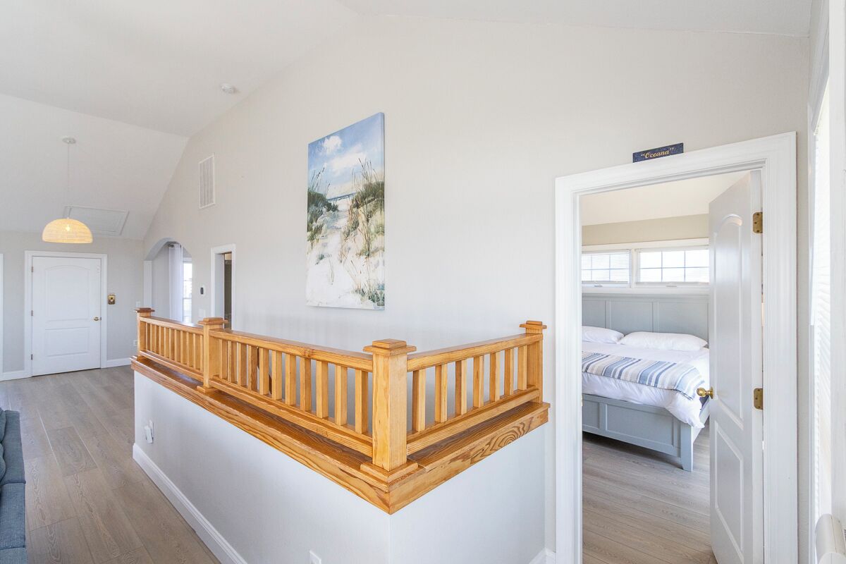 A room with a wooden staircase, a bed with striped bedding, and a painting on the wall.