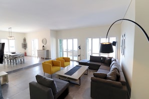 A modern living room with a sofa, chairs, a dining area, and a large window.