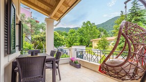 Un balcon agrémenté de meubles en osier, d’un fauteuil suspendu et offrant une vue sur des collines verdoyantes.