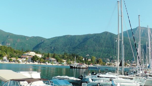 Un port de plaisance avec des bateaux amarrés, une plage et des montagnes en arrière-plan.