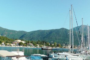 A marina with boats docked, a beach, and mountains in the background.