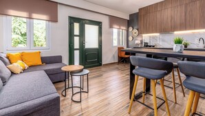 Un espace de vie moderne comprenant un canapé, des fauteuils, une petite table, un coin cuisine avec un bar et une porte verte.