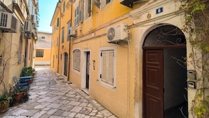 A narrow cobblestone street with buildings on either side, a brown door, and a blue sign with the number 6. - The Monastery apartment (Corfu)