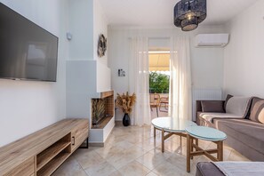 A modern living room with a flat-screen TV, a wooden bench, a glass table, a sofa, and a view of the outdoors.