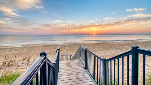 Une promenade en bois menant à une plage, avec un coucher de soleil en arrière-plan.