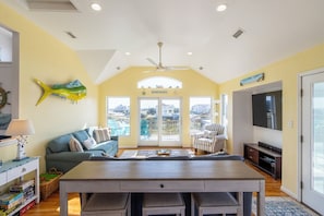 A living room with a sofa, a dining table, a TV, and a view through the glass doors.