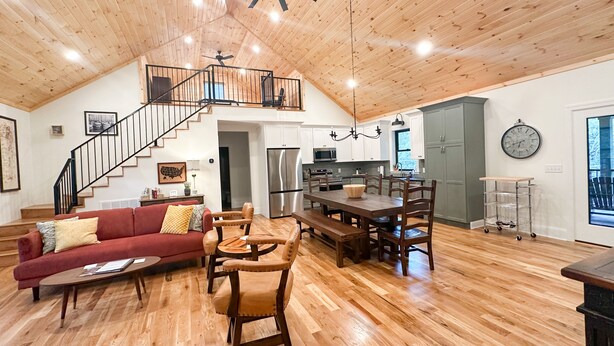 A spacious living area with a wooden ceiling, a dining table with chairs, a red sofa, and a staircase leading to an upper level.