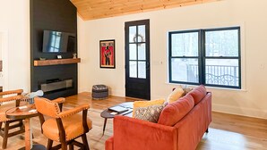 A living room with a wooden ceiling, a television, a sofa, and a dining area with chairs.
