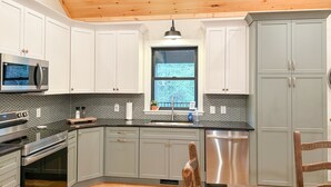 A modern kitchen with white cabinets, a stainless steel refrigerator, and a wooden ceiling.