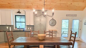 A dining area with a wooden table and benches, a chandelier, and a clock on the wall.