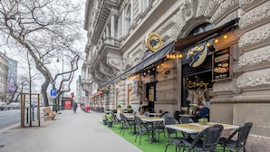 An outdoor cafe with tables and chairs on a green carpet, set against a historic building with ornate architecture. - Budapest Marvelous Apartment (Budapest)