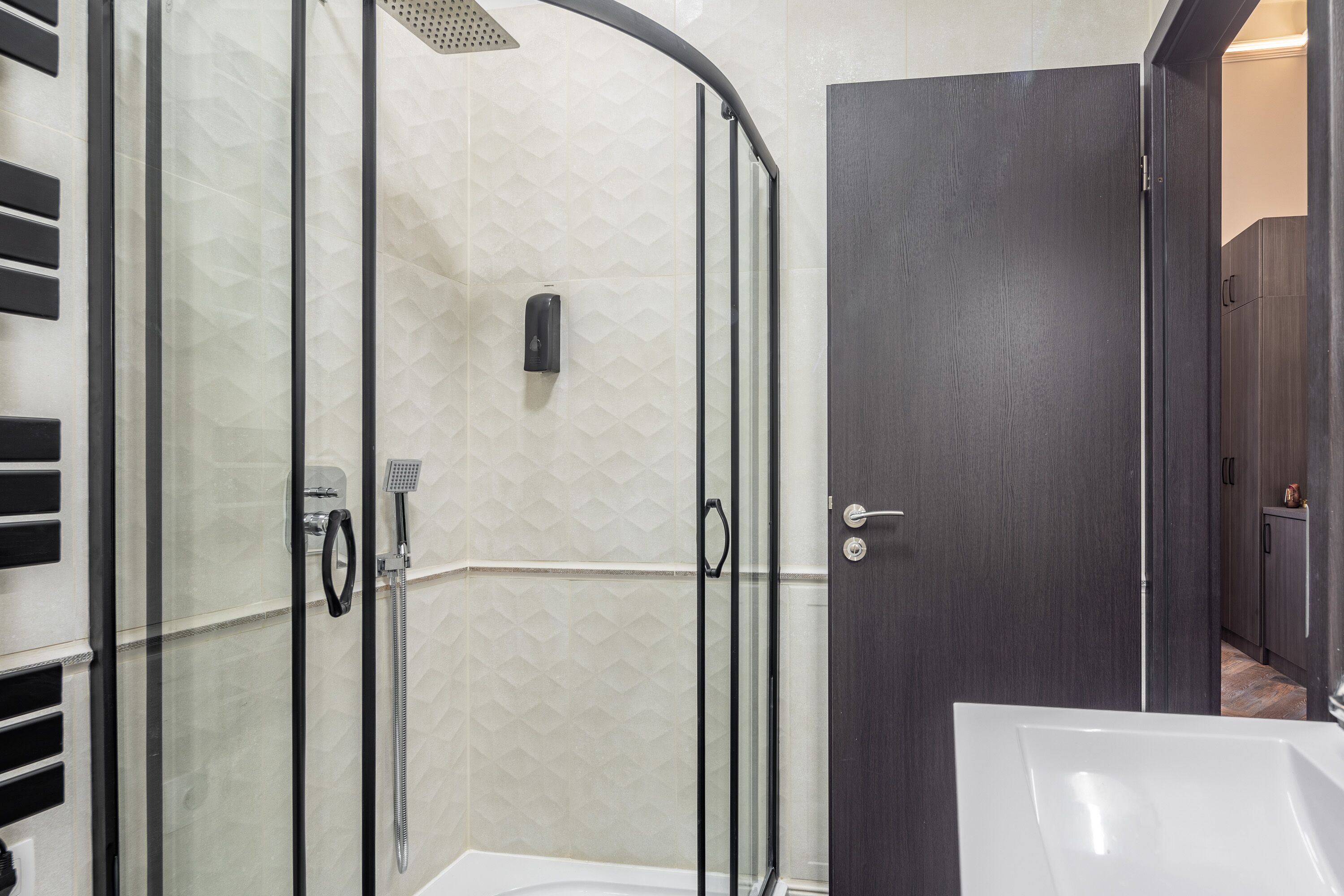 Ein modernes Badezimmer mit einer gläsernen Duschkabine, einem weißen Waschbecken und dunklen Holztüren.