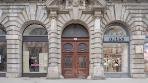 A historic building with a central arched entrance, a Guess store on the right, and a closed store on the left. - Budapest Marvelous Apartment (Budapest)