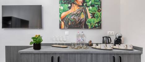 A modern kitchen with grey cabinetry, a flat-screen TV mounted above the counter, and a painting of a woman on the wall.
