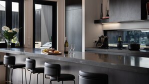 A modern kitchen with a bar area, bar stools, a wine bottle, and a coffee maker. - Chalet Noir- sleek design with heated plunge pool, close to town (Daylesford)