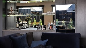 A modern bar area with a large window, a sofa with cushions, and various bar items including glasses and bottles. - Chalet Noir- sleek design with heated plunge pool, close to town (Daylesford)