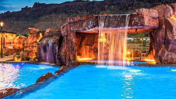 Una piscina con cascada, rodeada de formaciones rocosas y una zona de estar.
