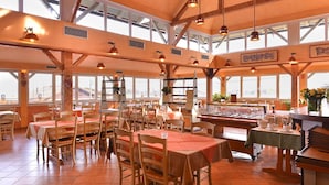 A spacious restaurant with high ceilings, large windows, and wooden beams. Tables are set with orange tablecloths and wooden chairs. - Pension Les (Brežice)