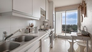 A modern kitchen with white cabinetry, a double sink, a stove, and a view of the city through large windows. - Superb balcony - Sea view - Apartment for 2 (La Baule-Escoublac)