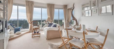 A spacious living room with a balcony, a dining area, and a bedroom with a large window.
