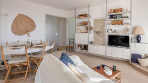 A living room with a white sofa, a dining table set with chairs, a TV, and shelves with decorative items. - Superb balcony - Sea view - Apartment for 2 (La Baule-Escoublac)