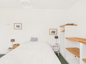 Une chambre à coucher au style minimaliste, avec un lit simple, deux tables de chevet, une lampe, un tableau encadré et une étagère en bois.