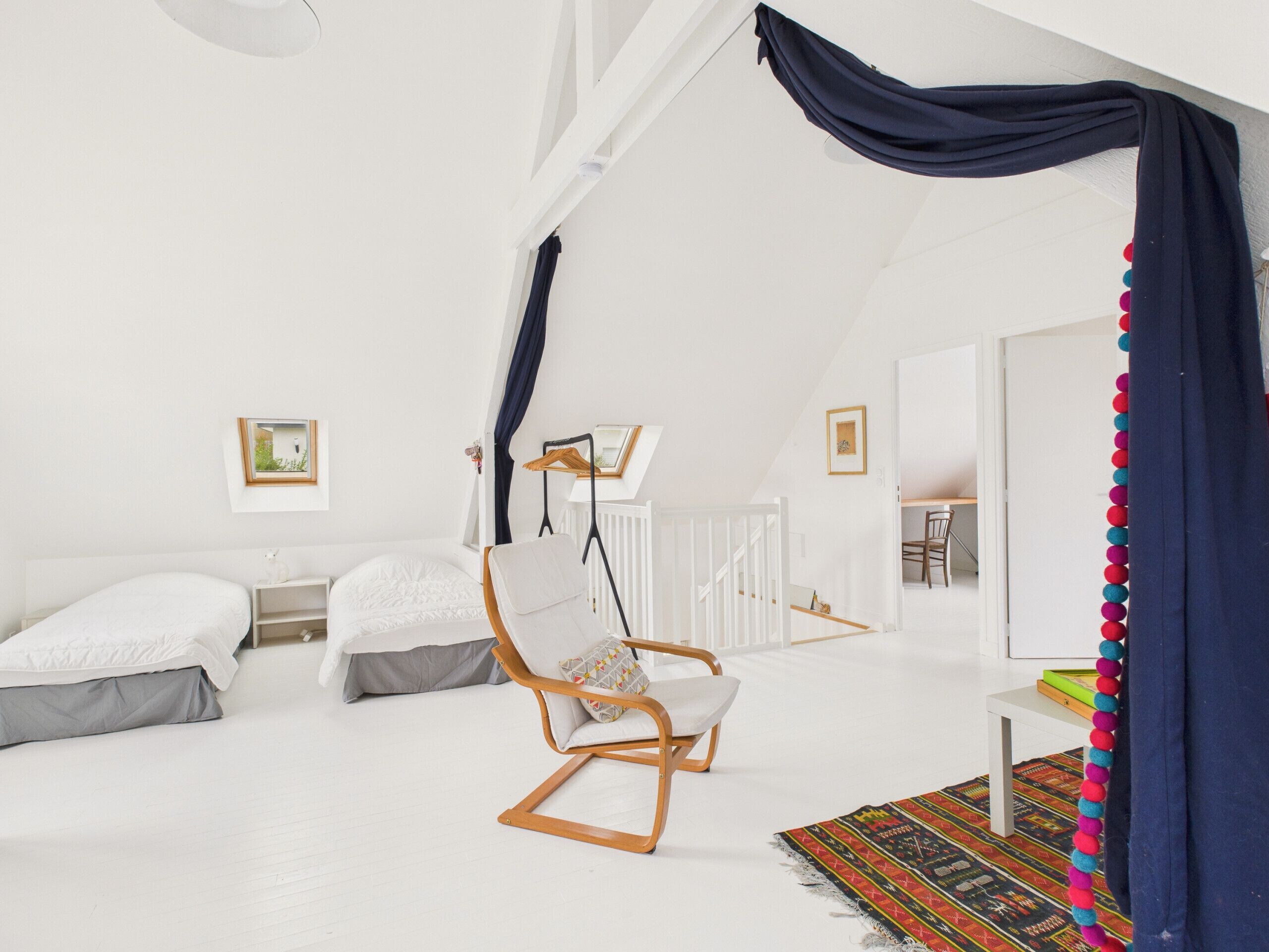 A bright, white room with a large bed, a wooden chair, and a colorful rug.