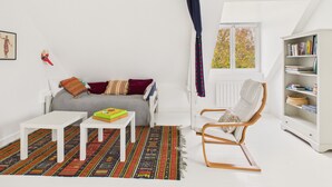 A cozy room with a white sofa, a small table, a rocking chair, and a bookshelf.